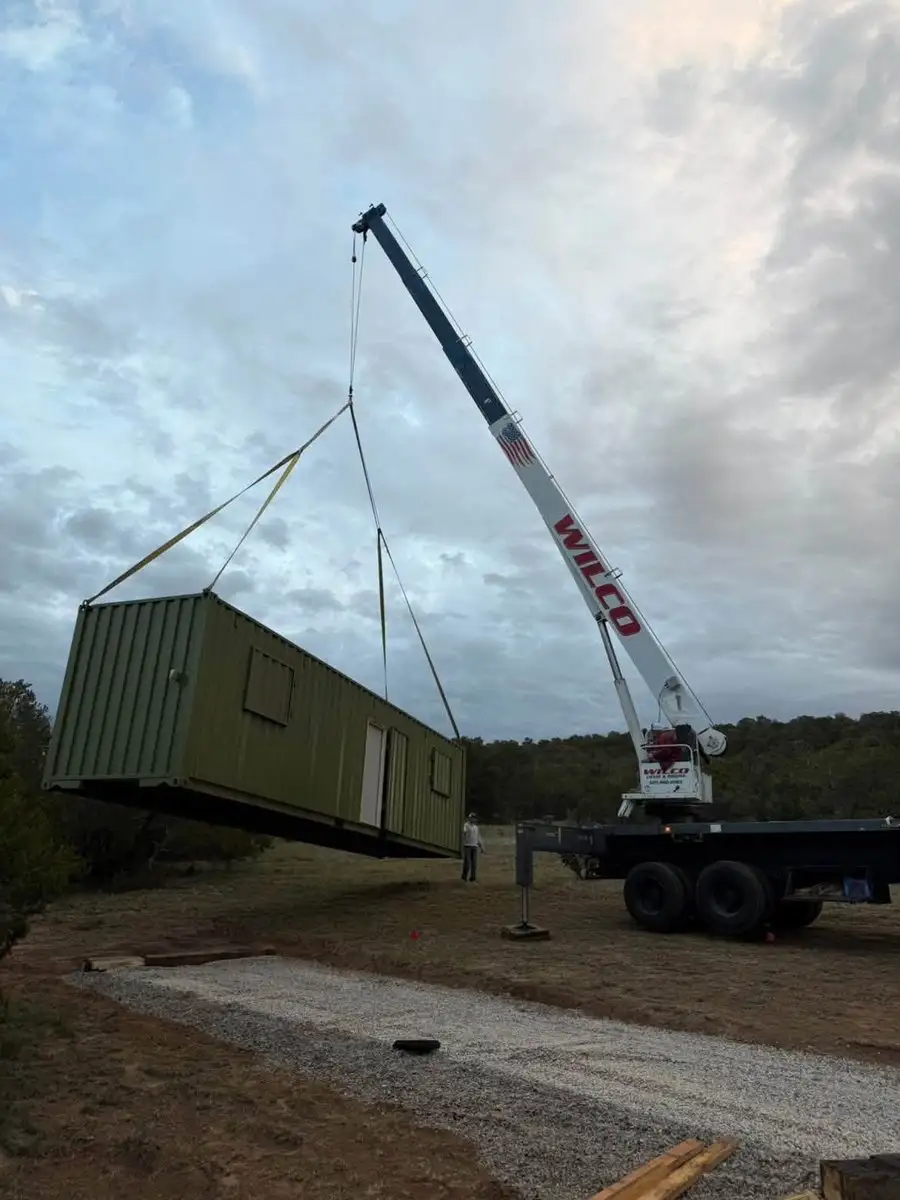 A shipping container lifted by crane onto a site prepared with a gravel pad