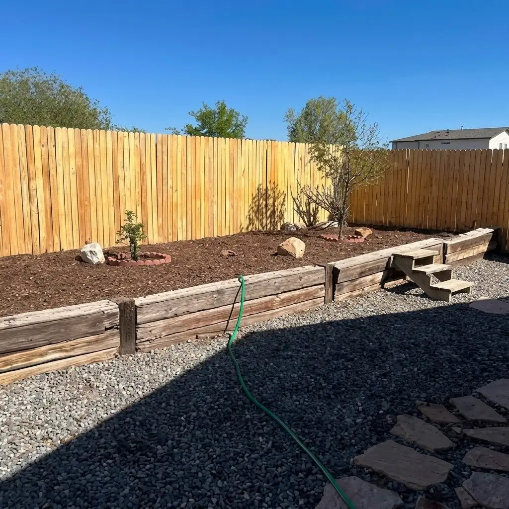 New wood privacy fence above a timber raised bed with mulch, boulders, gravel, and a flagstone path