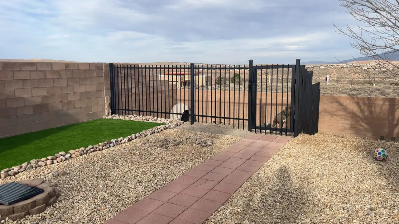 Turf and gravel beside a black metal fence and gate overlooking the mesa