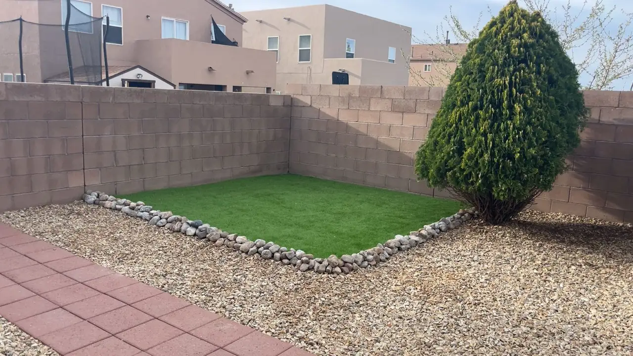 Artificial turf framed by a river rock border, with gravel and a paver path